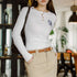 Person wearing a white long-sleeve shirt with a logo and beige pants in an indoor setting.